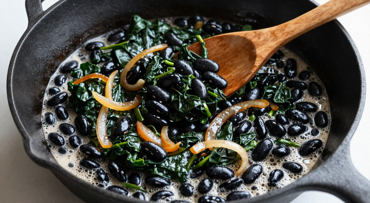 Black beans heating with wilted Swiss chard in a cast-iron skillet
